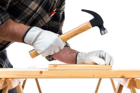 Close-up. Carpenter with his hands protected by gloves, with hammer and nails fixes a wooden board. Construction industry, do it yourself. White background.の写真素材
