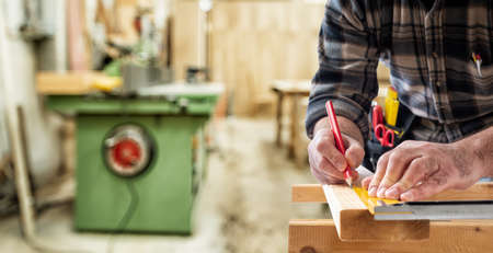 Close-up. Carpenter with pencil and carpenter's square draw the cutting line on a wooden board. Construction industry.の写真素材