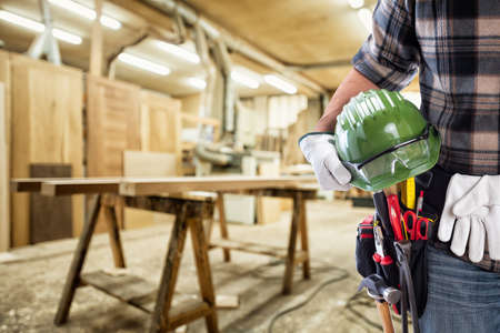 Close-up. Carpenter with hands protected by gloves holds helmet and protective goggles. Construction...