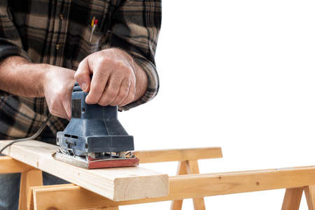 Close-up. Carpenter with the electric sander smoothes a wooden board. Construction industry. White background.の写真素材