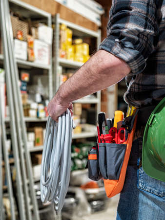 Electrician in the electrical parts store is holding the roll of electrical cable. Construction...