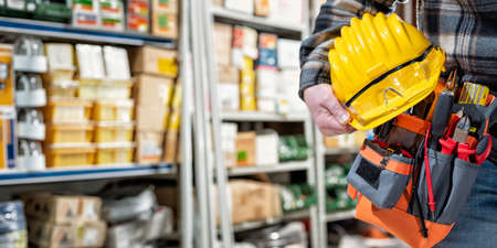 Electrician in the electrical component store holds the helmet and goggles in his hand. Construction industry, electrical system.の写真素材