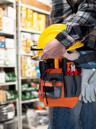 Electrician in the electrical component store holds the helmet and goggles in his hand. Construction...