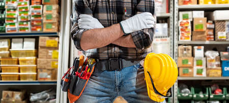 Carpenter electrician in the store of electrical components with arms crossed, he wears protective gloves. Construction industry, electrical system. の写真素材