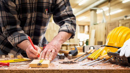 Close-up. Carpenter with pencil and the meter marks the measurement on a wooden board. Construction industry, carpentry workshop.の写真素材