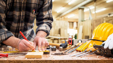 Close-up. Carpenter with pencil and carpenter's square draw the cutting line on a wooden board. Construction industry, carpentry workshop.の写真素材