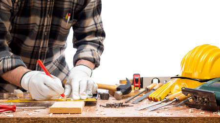 Close-up. Carpenter with his hands protected by gloves with pencil and carpenter's square draw the cutting line on a wooden board. Construction industry. Isolated on a white background.の写真素材