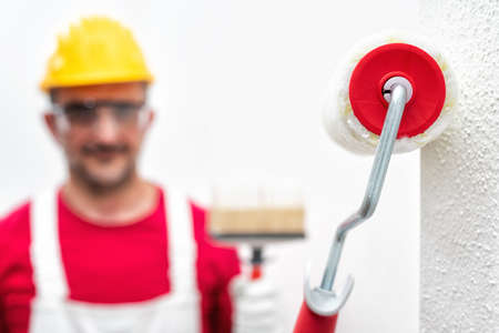 Close-up of the paint roller, in the background house painter at work painting the white wall. Construction industry. Work tools.の写真素材