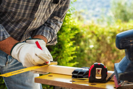 Close-up. Carpenter with his hands protected by gloves with pencil and carpenter's square draw the cutting line on a wooden board. Construction industry. Work safety.の写真素材