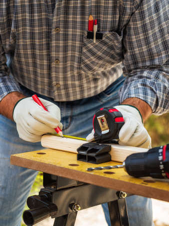 Close-up. Carpenter with his hands protected by gloves with pencil and the meter marks the measurement on a wooden board. Construction industry. Work safety.の写真素材