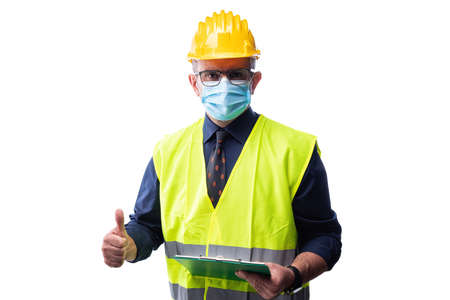 Engineer isolated on white background wears surgical mask to prevent Coronavirus spread, makes OK sign with thumb up. Preventing Pandemic Covid-19 at the workplace.の写真素材