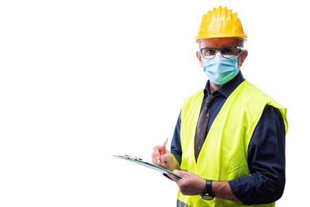 Engineer isolated on white background wears surgical mask to prevent Coronavirus spread, holds pen and notebook in hand. Preventing Pandemic Covid-19 at the workplace.の写真素材