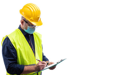 Engineer isolated on white background wears surgical mask to prevent Coronavirus spread, holds pen and notebook in hand. Preventing Pandemic Covid-19 at the workplace.の写真素材