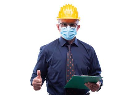 Engineer isolated on white background wears surgical mask to prevent Coronavirus spread, makes OK sign with thumb up. Preventing Pandemic Covid-19 at the workplace.の写真素材
