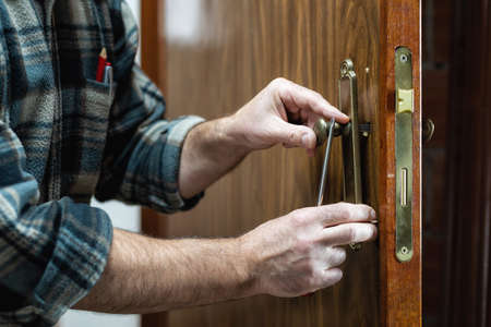 Close-up. Carpenter installs the lock handle of a wooden door. Construction industry.の写真素材