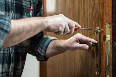 Close-up. Carpenter with screwdriver fixes the lock handle of a wooden door. Construction industry.の写真素材