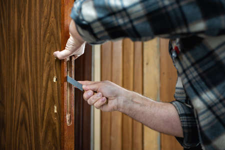 Close-up. Carpenter with the rasp prepares the hole for the lock of a wooden door. Construction industry.の写真素材