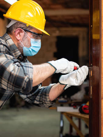 Carpenter worker at work repairs and installs a room door, wear the surgical mask to prevent Coronavirus infection. Preventing Pandemic Covid-19 at the workplace. Carpentry.の写真素材