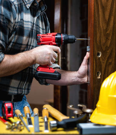 Close-up. Carpenter with an electric screwdriver fixes the lock of a wooden door. Construction industry.の写真素材