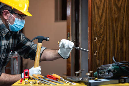 Carpenter worker at work repair and install a room door lock, wear the surgical mask to prevent Coronavirus infection. Preventing Pandemic Covid-19 at the workplace. Carpentry.の写真素材