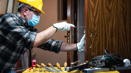 Carpenter worker at work repair and install a room door lock, wear the surgical mask to prevent Coronavirus infection. Preventing Pandemic Covid-19 at the workplace. Carpentry.の写真素材
