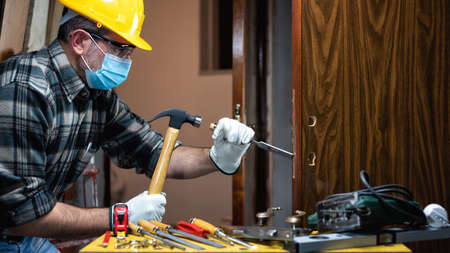Carpenter worker at work repair and install a room door lock, wear the surgical mask to prevent Coronavirus infection. Preventing Pandemic Covid-19 at the workplace. Carpentry.の写真素材