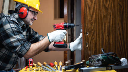 Close-up. Carpenter at work repairs and installs the new lock of a wooden door. Construction industry.の写真素材