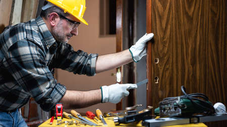 Close-up. Carpenter at work repairs and installs the new lock of a wooden door. Construction industry.の写真素材