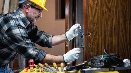 Close-up. Carpenter at work repairs and installs the new lock of a wooden door. Construction industry.の写真素材