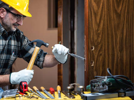 Close-up. Carpenter at work repairs and installs the new lock of a wooden door. Construction industry.の写真素材