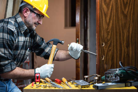 Close-up. Carpenter at work repairs and installs the new lock of a wooden door. Construction industry.の写真素材
