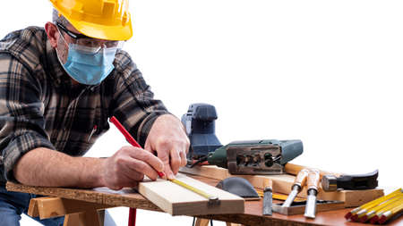 Carpenter worker at work isolated on white background, wears helmet, goggles and surgical mask to prevent  infection.の写真素材