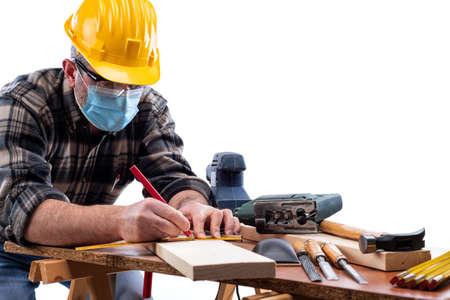 Carpenter worker at work isolated on white background, wears helmet, goggles and surgical mask to  coronavirus infection.の写真素材