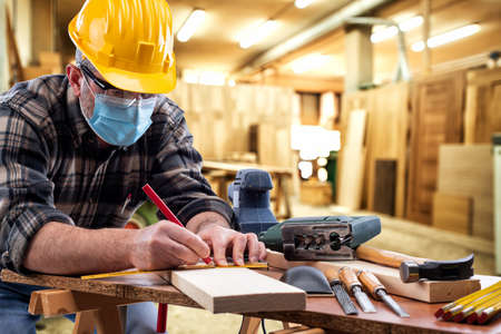 Carpenter worker at work in the carpentry workshop, wears helmet, goggles and surgical mask to prevent  infection.の写真素材
