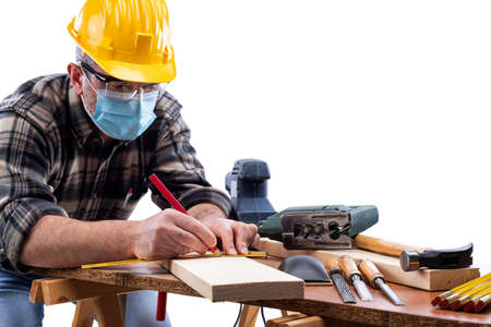 Carpenter worker at work isolated on white background, wears helmet, goggles, leather gloves and surgical mask to prevent infection.の写真素材