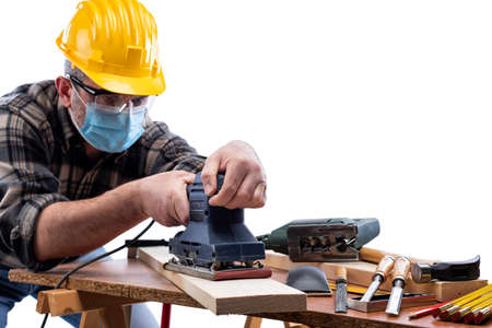Carpenter worker at work isolated on white background, wears helmet, goggles, leather gloves and surgical mask to prevent coronavirus infection.の写真素材