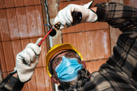 Electrician worker at work replaces the lamp holder protected by helmet, safety goggles and glovesの写真素材