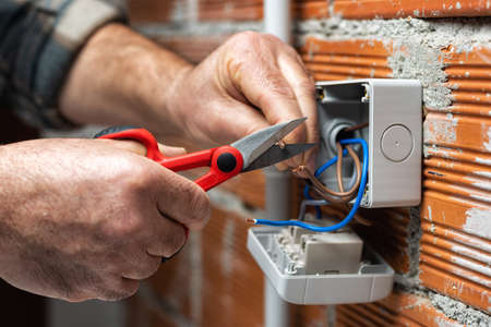 Electrician worker at work with scissors prepares electrical cables of a residential electrical...