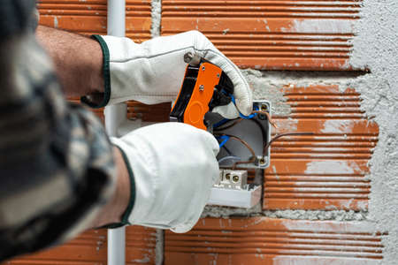 Electrician worker at work with wire stripper prepares electrical cables of a residential electrical system. Working safely with protective gloves. Construction industry.の写真素材