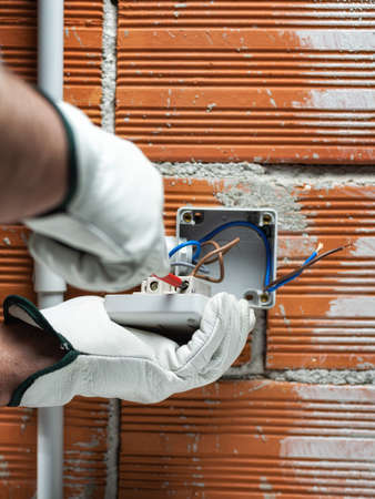 Electrician worker at work with a screwdriver fixes the cable in the terminal of the switch of a residential electrical system. Working safely with protective gloves. Construction industry.の写真素材