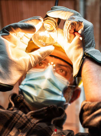 Electrician worker at work replaces the light bulb protected by helmet, safety goggles and gloves. Wear the surgical mask to prevent the spread virusの写真素材