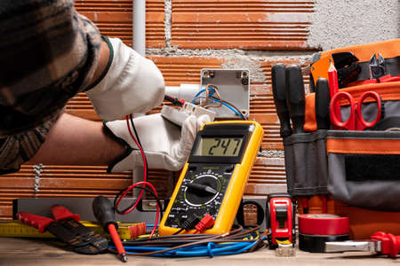 Electrician worker at work with the tester measures the voltage in an electrical system. Working safely with protective gloves. Construction industry.の写真素材