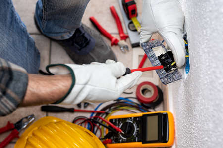 View from top. Electrician worker with screwdriver fixes electrical cables in the terminals of the socket of an electrical system. Working safely with protective gloves. Construction industry.の写真素材