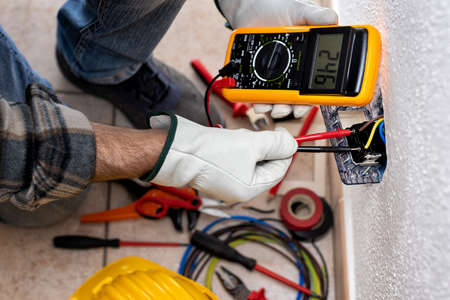 View from above. Electrician worker at work with the tester measures the voltage in an electrical system. Working safely with protective gloves. Construction industry.の写真素材