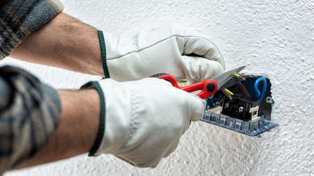 Electrician worker at work with scissors prepares the electrical cables of an electrical system. Working safely with protective gloves. Construction industry.の写真素材