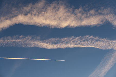 Landscape of a beautiful blue sky with clouds, white vapor trails and a plane in the evening. Nature.の写真素材