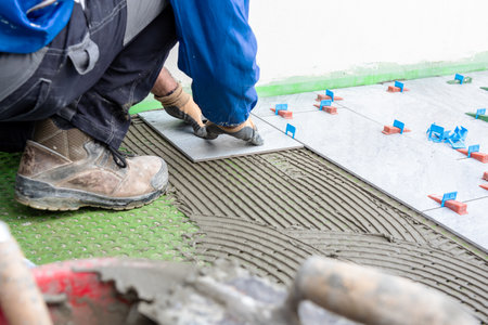 Bricklayer tiler places tiles of a new floor on the glue. Construction industry. Building.の写真素材