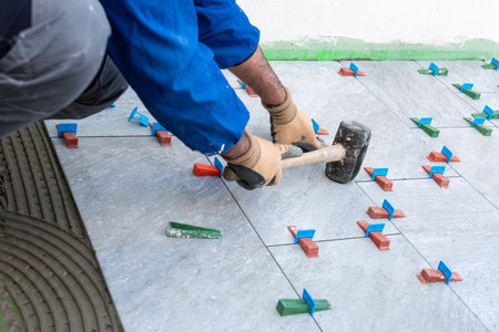 Bricklayer tiler with hammer puts in place the tiles of a new floor. Construction industry. Building.の写真素材