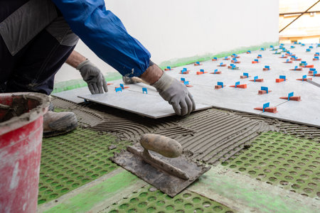 Bricklayer tiler places tiles for a new floor on cement glue. Construction industry. Building.の写真素材
