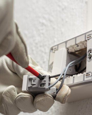 Electrician worker with screwdriver fixes electrical wires in the terminals of the diverter switch of an electrical system. Working safely with protective gloves. Construction industry.の写真素材